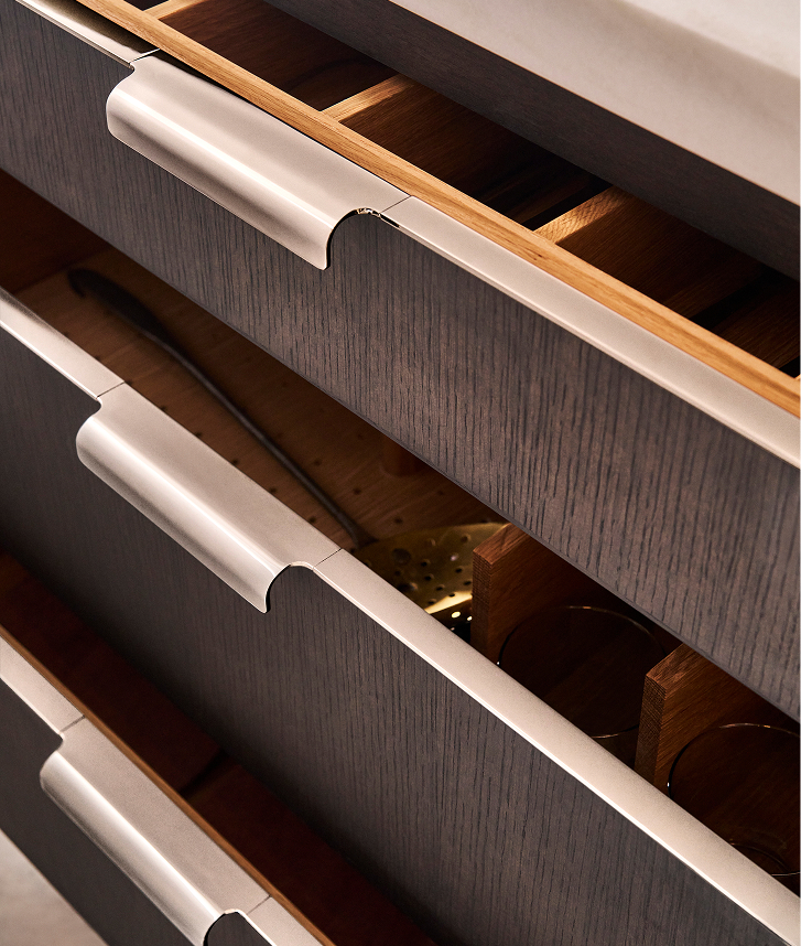 A blend of functionality and ornamentation, precision-applied brass clads the drawer edge and extends seamlessly to form an integrated pull.